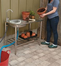 a woman holding a potted plant next to a metal table with pots on it