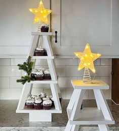 two white shelves with cupcakes and star lights on them in the shape of christmas trees