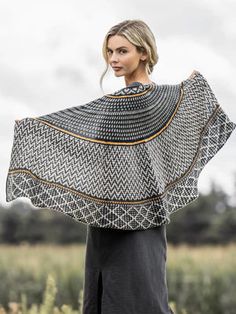 a woman is standing in a field with an open shawl over her shoulders and looking at the camera