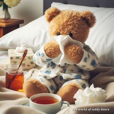 a teddy bear sitting on top of a bed next to a cup of tea and honey