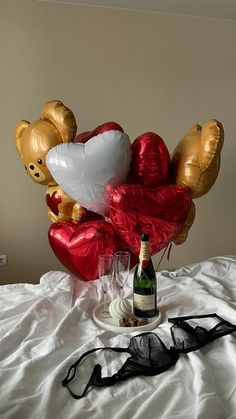 a bottle of champagne and some balloons in the shape of teddy bears on a bed