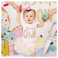 a baby girl wearing a pink and yellow dress holding a donut in her hand