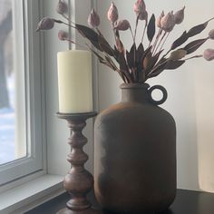 a vase with some flowers in it next to a candle on a window sill