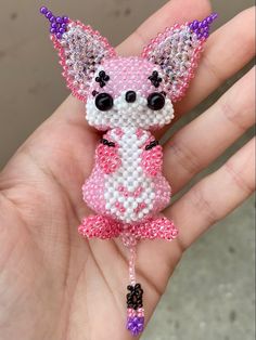 a hand holding a small pink and white beaded animal