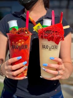 two women holding up drinks with straws on them and one has blue nail polish