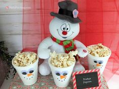 a snowman with popcorn buckets in front of it and a sign on the table