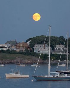 a full moon is seen over boats in the water and houses on the other side