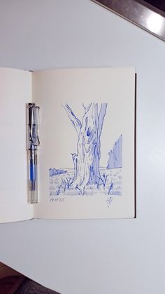 an open book with a pen on top of it next to a drawing of a tree