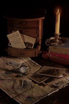 a table topped with lots of books next to a lit candle and a clock on top of it