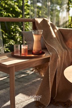 a wooden bench with two glasses on it and a blanket draped over the bench next to it