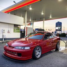 a red car is parked in front of a gas station with its hood open and no fuel