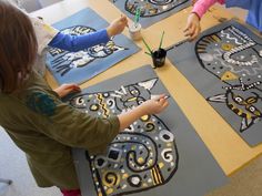 three children sitting at a table painting pictures on canvases with black and white cats