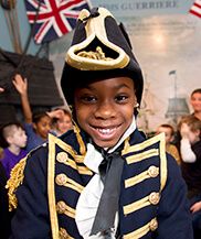 a young boy dressed in uniform and smiling for the camera with other children behind him