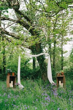 an outdoor ceremony set up in the woods with white draping and purple flowers