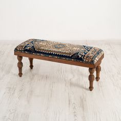 a wooden bench with a blue and white cushion on it's back end sitting on a wood floor