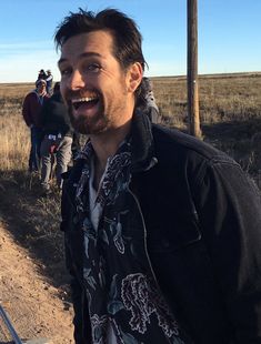 a man standing in the middle of a dirt road with people walking behind him on a sunny day