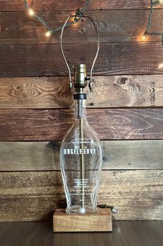 an empty glass bottle sitting on top of a wooden table next to a string of lights