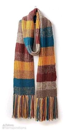 a multicolored scarf with fringes hanging on a white wall in front of it