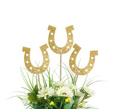 a vase filled with flowers and two gold horseshoes on top of each other in front of a white background