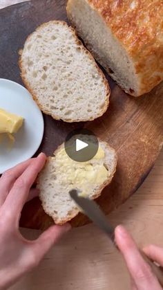 a person cutting bread on top of a wooden cutting board with butter and butter knife