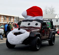 a jeep driving down the street with a santa hat on top of it's head