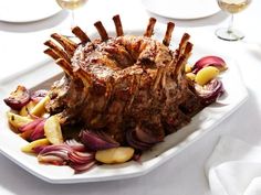 a large piece of meat on a white platter with onions and apples next to wine glasses