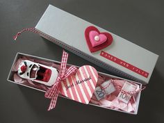 a pink and white gift box with two baby shoes in it next to a red heart