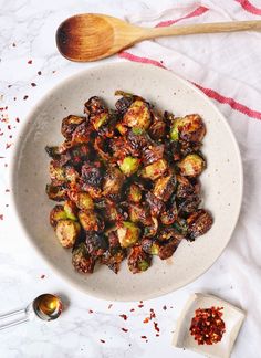 a white bowl filled with brussel sprouts next to a wooden spoon