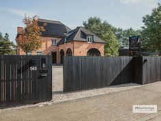 a black gate is in front of a large brick building with trees and bushes around it