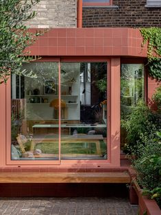 an orange house with large glass windows and wooden bench in the foreground, surrounded by greenery