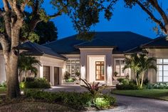 a large house with lots of trees and bushes in front of it at night time