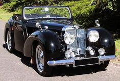 an old fashioned black car is parked on the side of the road in front of some trees