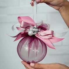 a hand holding a christmas ornament with pink ribbon and pearls on it's side