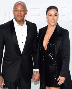 a man and woman standing next to each other in front of a white wall holding hands