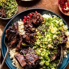 a blue plate topped with meat and rice next to bowls of vegetables on a wooden table