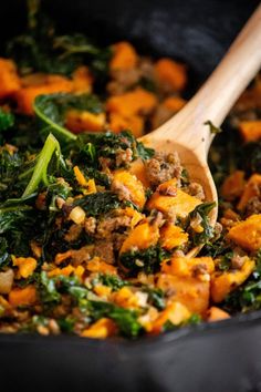 a skillet filled with vegetables and meat on top of a wooden spoon in it