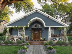 a blue house with white trim on the front door and porch is surrounded by greenery