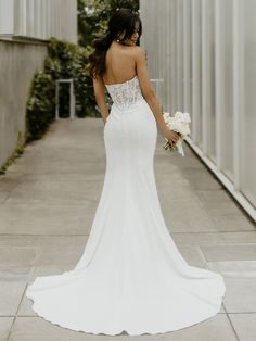 a woman in a white wedding dress is walking down the street with her back to the camera