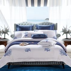 a bed with blue and white comforters in front of a window overlooking the ocean