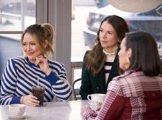 three women sitting at a table talking and drinking coffee