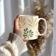 a person holding a coffee cup with green leaves on it