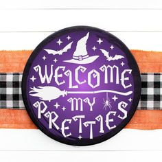 a purple and black welcome badge with white writing on an orange striped belt that says,'welcome my pretties '