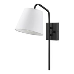 a black wall light with a white shade on the arm and a lamp attached to it