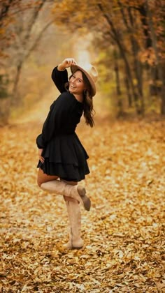 a woman in black dress and hat running through leaves