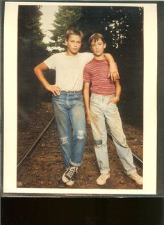 two young boys standing next to each other on train tracks with trees in the background