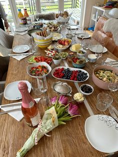 a wooden table topped with lots of plates and bowls filled with food next to wine glasses