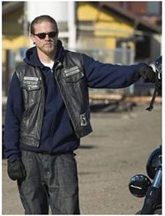 a man in black jacket and sunglasses standing next to a motorcycle with his hand out