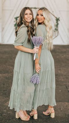 two beautiful women standing next to each other holding lavender flowers in their hands and smiling at the camera