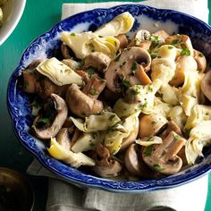 a blue bowl filled with pasta and mushrooms on top of a green table next to silverware