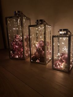 three glass containers with ornaments in them sitting on a wooden table next to a wall